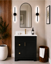 Pearl 30" black bathroom vanity with two drawers, gold hardware and white quartz countertop, styled in a modern bathroom with wood slat accent wall